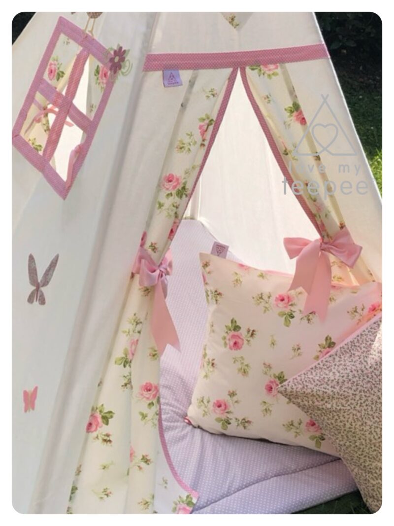 Close-up of Country Girl Pink & Cream teepee showing appliquéd butterflies, window with curtains, rose-print doors trimmed in pink with ribbon tie backs, and coordinating rose-print cushions with padded floor mat.