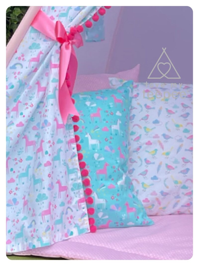 Close-up of the teepee doors showing unicorn, rainbow, and cloud pattern, trimmed with pink pom-poms. Includes matching scatter cushions and a padded floor mat.