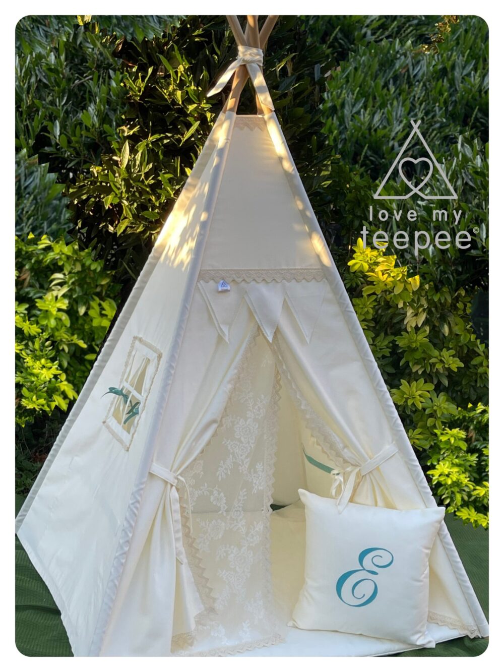 Handmade Personalised kid’s teepee in classic ivory, featuring lace doors tied with ivory ribbons, pom-pom edging, and coordinating scatter cushion with embroidered initial.